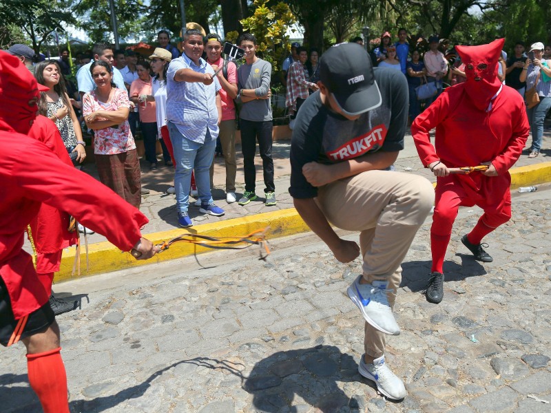 Als Dämonen verkleidete Schauspieler peitschen einen jungen Mann aus. Hier handelt es sich um die traditionelle Zeremonie „Los Talciguines“, die den Beginn der Karwoche in El Salvador (Zentralamerika) markiert. 