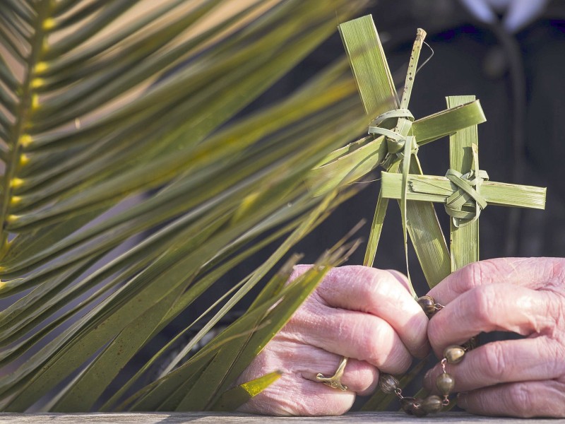 Eine Frau hält bei der Messe am Palmsonntag auf dem Petersplatz im Vatikan (Italien) einen Rosenkranz und zwei aus Palmenblättern geformte Kreuze in der Hand.