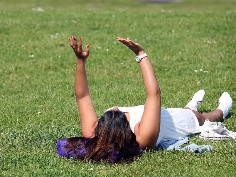 Hallo Sonne! Eine junge Frau sonnt sich auf dem Rasen der Rheinpromenade in Düsseldorf  und streckt dabei die Hände gen Himmel.