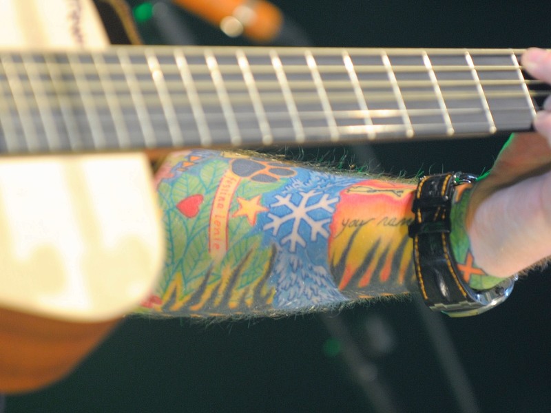 Ein bunter Arm und eine Gitarre. Welchem Musiker gehört wohl dieses farbenfrohe Kunstwerk?