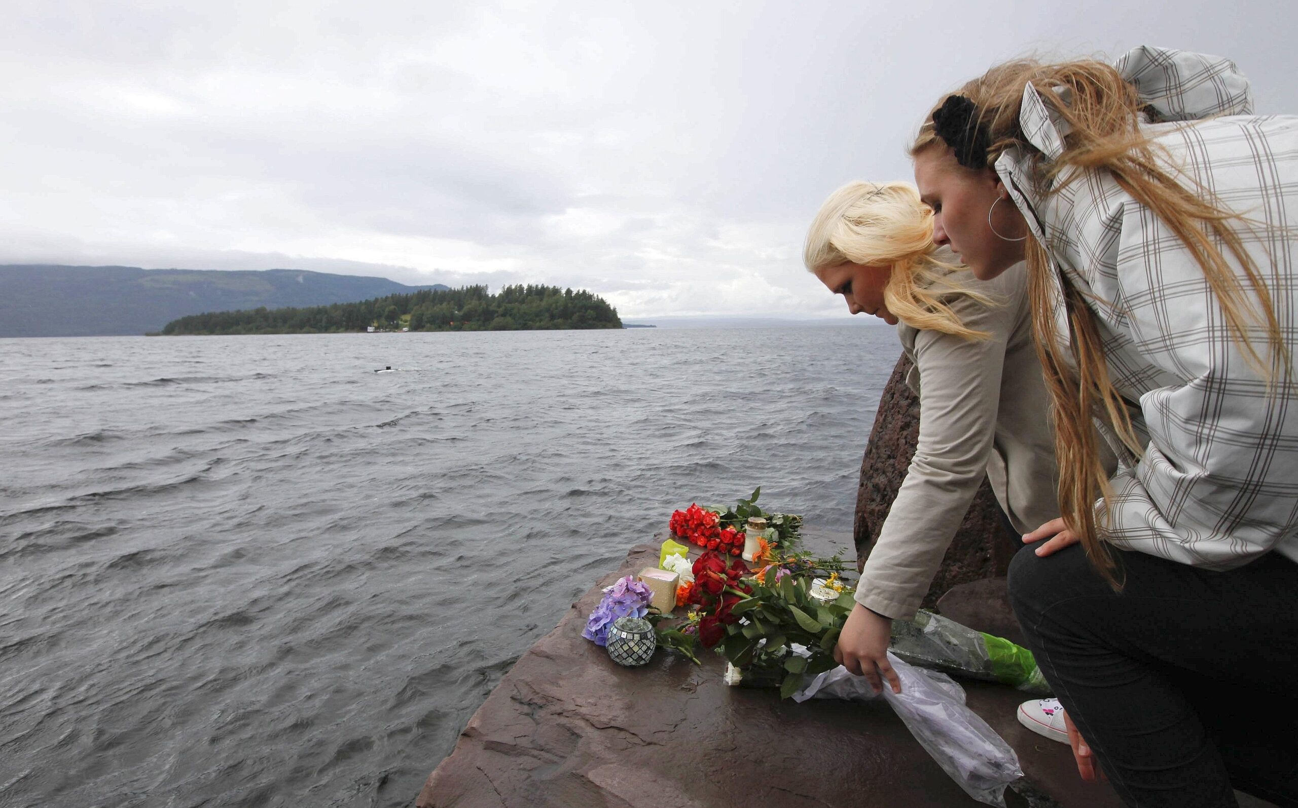 Zwei junge Frauen legen Blumen ans Ufer gegenüber der Insel Utöya.