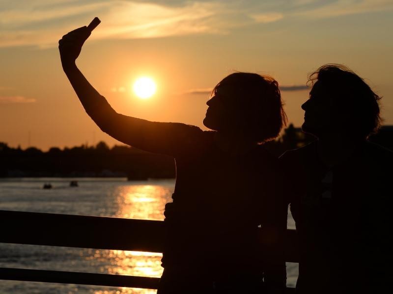 Ein glühender Sonnenuntergang, der sich im Wasser spiegelt, davor ein verliebtes Pärchen. Mehr braucht es für ein "Relfie" nicht.