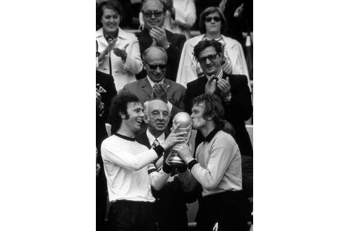 Franz Beckenbauer hält den WM-Pokal Sepp Maier hin, der ihn jubelnd küsst.