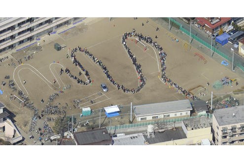 Auf einem Schulhof in Sendai hat sich eine lange Schlange gebildet. Die Menschen stehen hier...