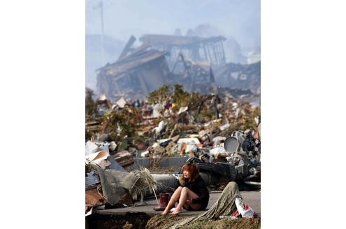 Eine Frau sitzt unter Schock in den Trümmern der Stadt Natori.