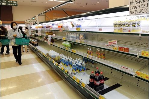. . . sind viele Lebensmittelläden nach Panikkäufen der Bevölkerung leer. Ein Mann mit Atemschutzmaske sucht in den leeren Regalen eines Supermarkts in Akita nach Mineralwasser. Es gibt keins mehr.