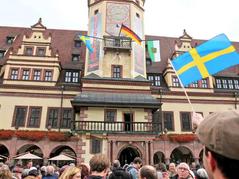 Ein Mann mit schwedischer Fahne wartet auf die Ankunft des schwedischen Königspaares vor dem Alten Rathaus in Leipzig.