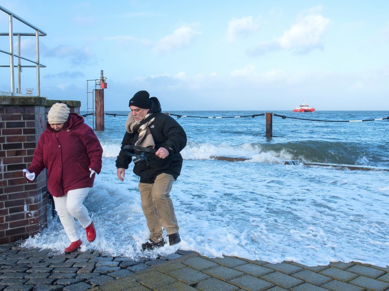 Bereits am Montag hatte es stürmische Winde gegeben, wie hier in Cuxhaven. Zwei Weihnachtsspaziergänger flüchten vor einer herranrollenden Welle.