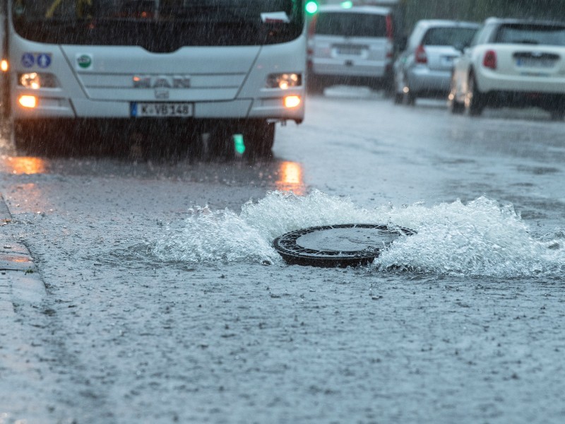 Der Deckel eines Gullys wurde auf einer überfluteten Straße in Köln vom Wasserdruck hochgehoben. 