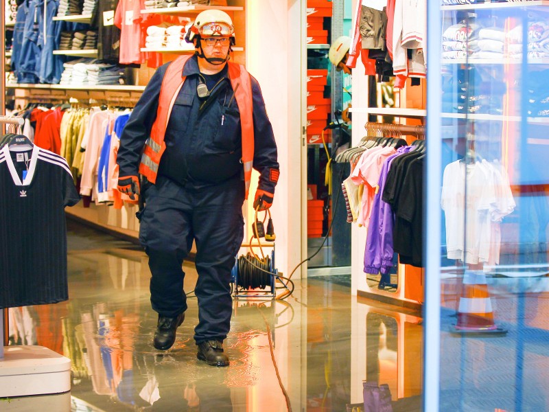 Ein Feuerwehrmann läuft durch ein überflutetes Bekleidungsgeschäft in einem Einkaufszentrum. 