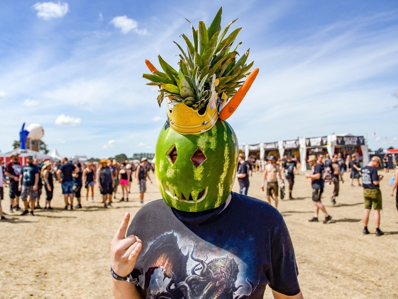 Ein Festivalbesucher hat sich einen Helm aus einer Wassermelone, zwei Mohrrüben und einer Ananas gebastelt. 