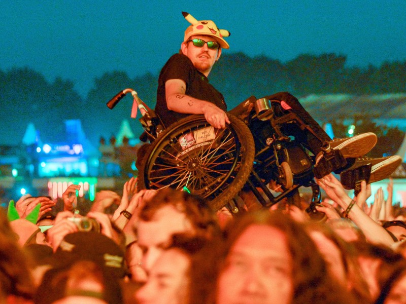 Fans halten zusammen. Ein Metal-Fan im Rollstuhl wird während eines Konzerts von anderen Fans auf Händen getragen. 