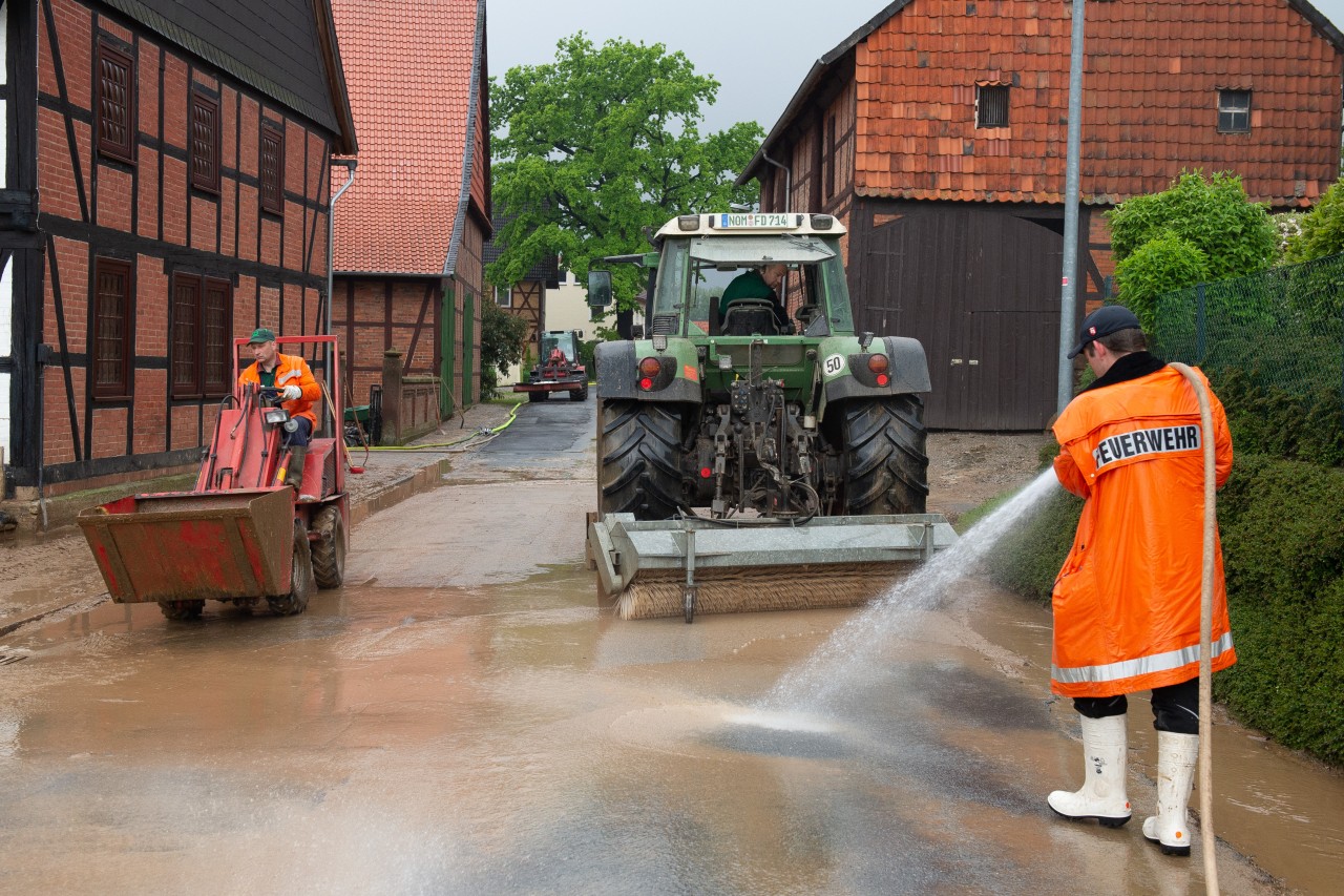 Bad Gandersheim: Einsatzkräfte der Feuerwehr reinigen mit Wasserschläuchen eine Durchgangsstraße in Bad Gandersheim im Ortsteil Ackershausen. Tief "Axel" hat in Südniedersachsen in der Nacht für starke Regenfälle und teilweise für Überschwemmungen gesorgt. 