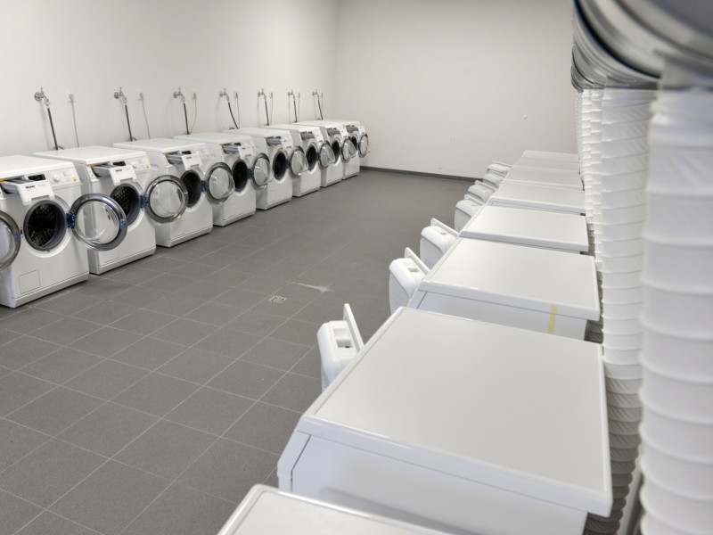 Ein Raum mit zahlreichen Waschmaschinen und Trocknern dient als Wäscherei.