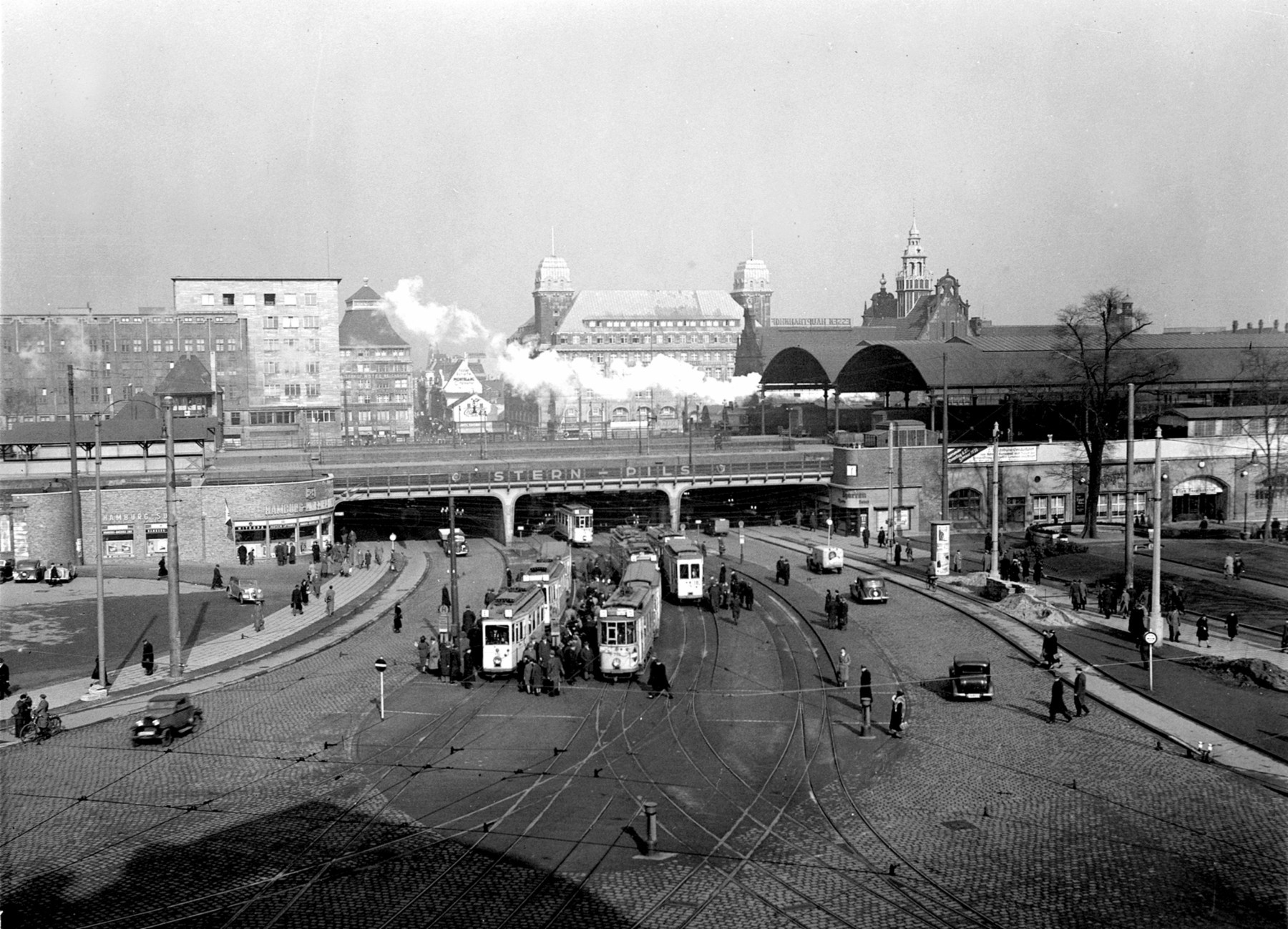 Die Freiheit um 1939 - schon mit Autos, aber anders als heute noch mit Straßenbahnen. Im Hintergrund (v.li.): die Hauptpost, das Eick-Haus (heute Ansons), das Hotel Handelshof und der Turm des im Weltkrieg zerstörten alten Hauptbahnhofs. Gerade fährt eine Dampflok los.