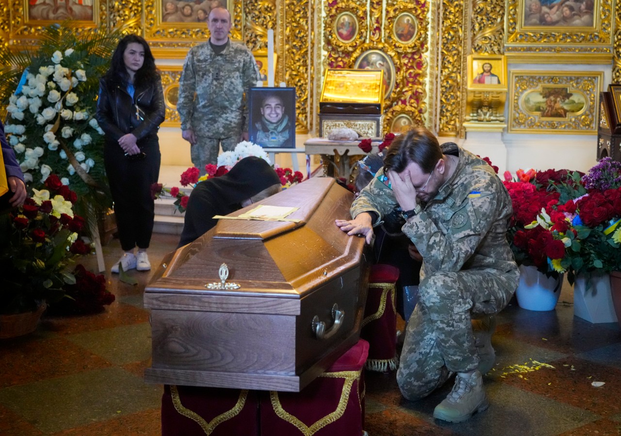 09.05.2022, Ukraine, Kiew: Ein Soldat kniet während der Beerdigung in der St. Michael Kathedrale am Sarg des im Einsatz gefallenen freiwilligen Soldaten Oleksandr Makhov, der zu den bekanntesten ukrainischen Journalisten gehörte.