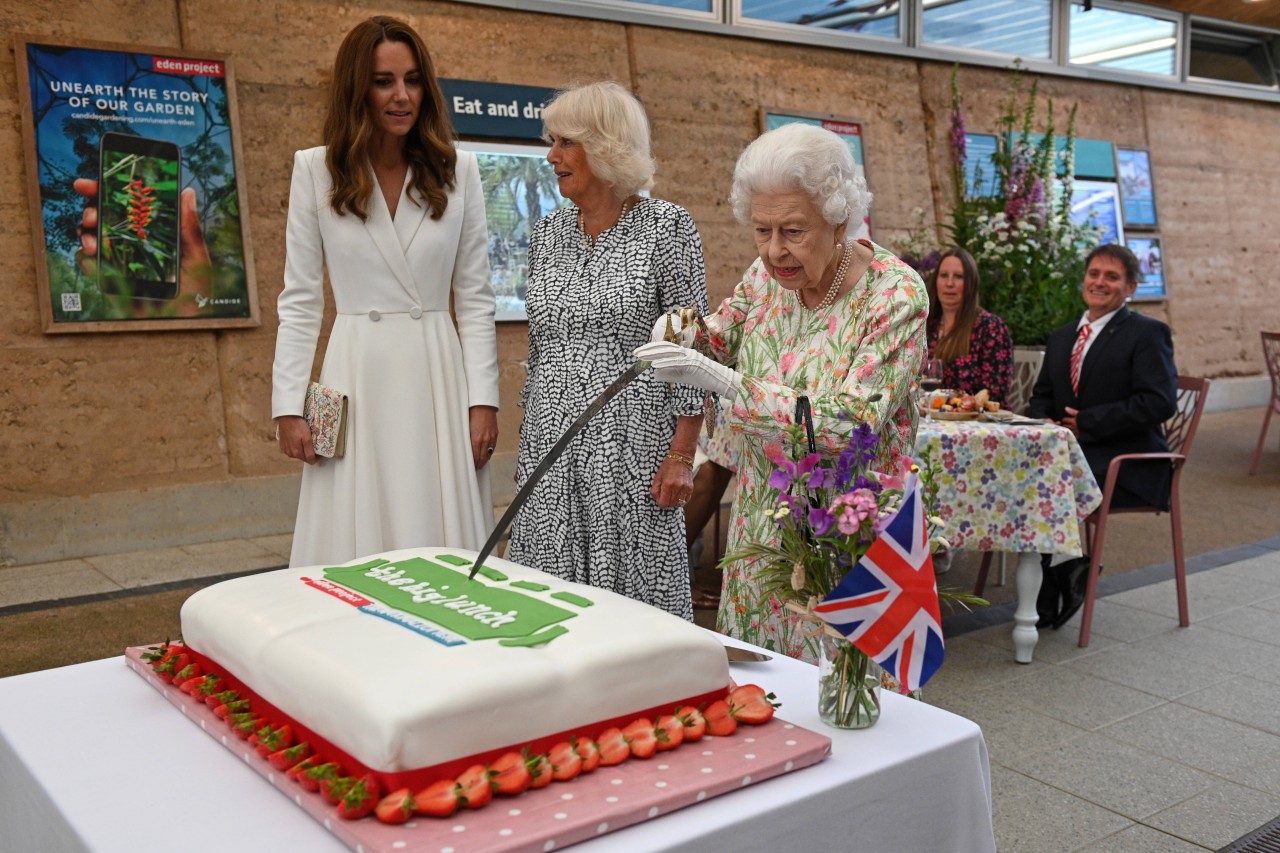 Queen Elizabeth II. versucht mit einem Messer einen Kuchen anzuschneiden.