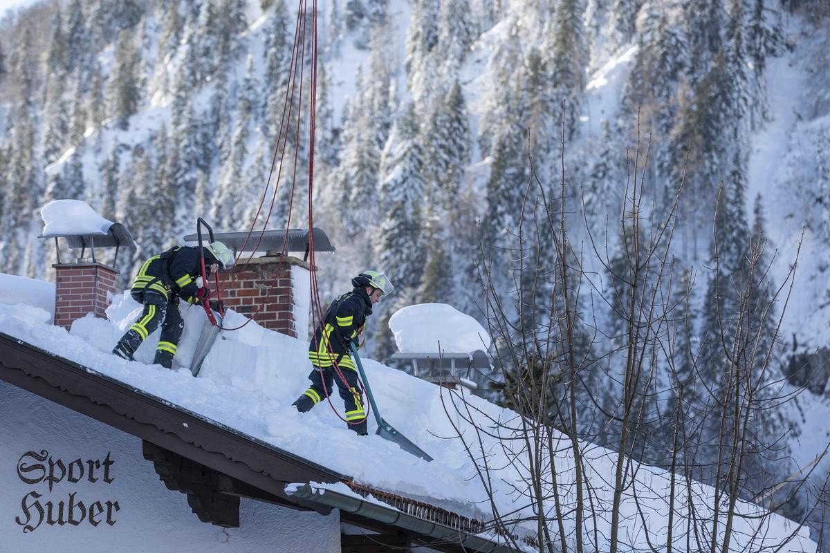Feuerwehrleute räumen auf einem Haus in Bayrischzell im Grenzgebiet zu Österreich Schnee von einem Dach. Dennoch sprechen Meteorologen von keiner außergewöhnlichen Wetterlage.