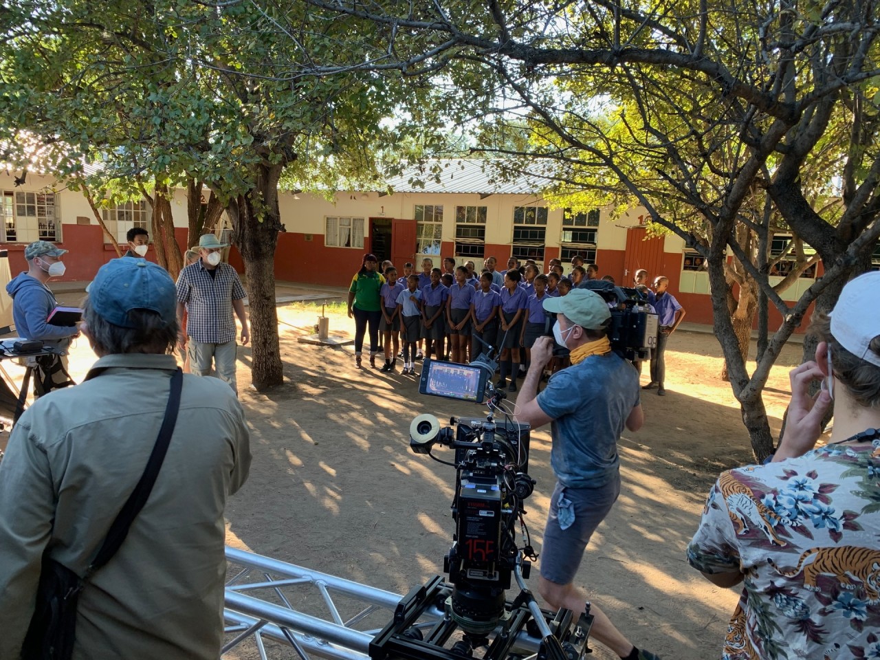 Das ZDF-Filmteam dreht auf einem Schulhof im Norden Namibias. Auch eine Gruppe von Schülern in blauen Uniformen ist anwesend.