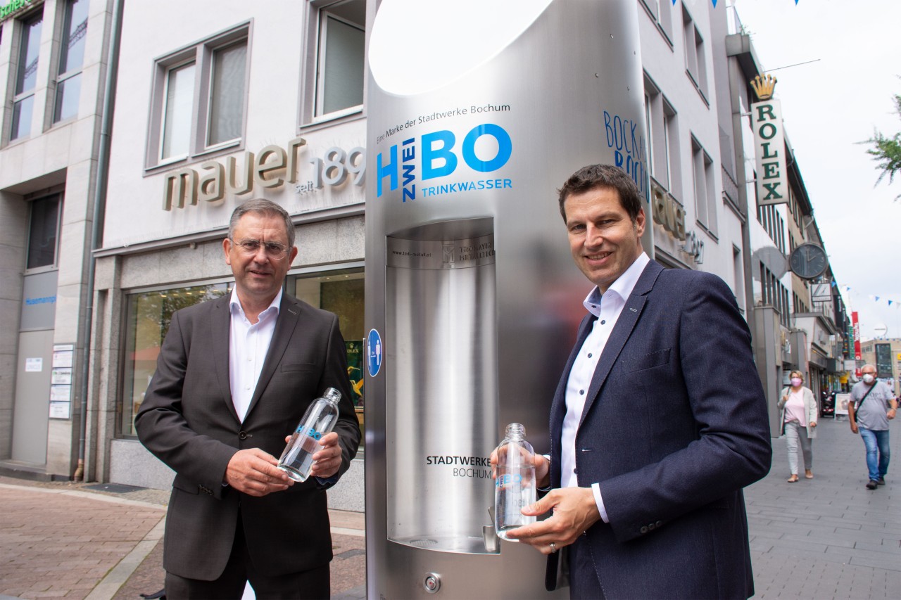 Bochum: Oberbürgermeister Thomas Eiskirch (rechts) und Stadtwerke-Geschäftsführer Dietmar Spohn (links) nehmen den mobilen Trinkwasserspender auf dem Husemannplatz in Betrieb.