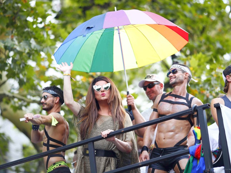 Diese Feiernden schützen sich mit einem Regenbogen-Sonnenschirm vor der Sonne.