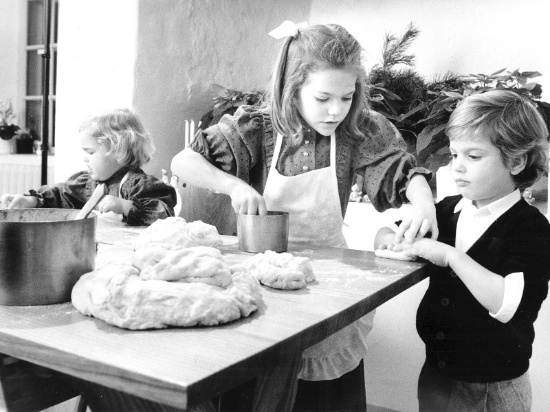 In der Weinachtsbäckerei: Victoria zeigt ihrem jüngeren Bruder Prinz Carl Philip (r.), wie der Plätzchenteig am besten zu formen ist. Schwester Prinzessin Madeleine (l.) weiß, wie es geht. Die schwarz-weiß Aufnahme entstand am 12. Dezember 1984, am Tag vor dem in Schweden wichtigen Luciafest.