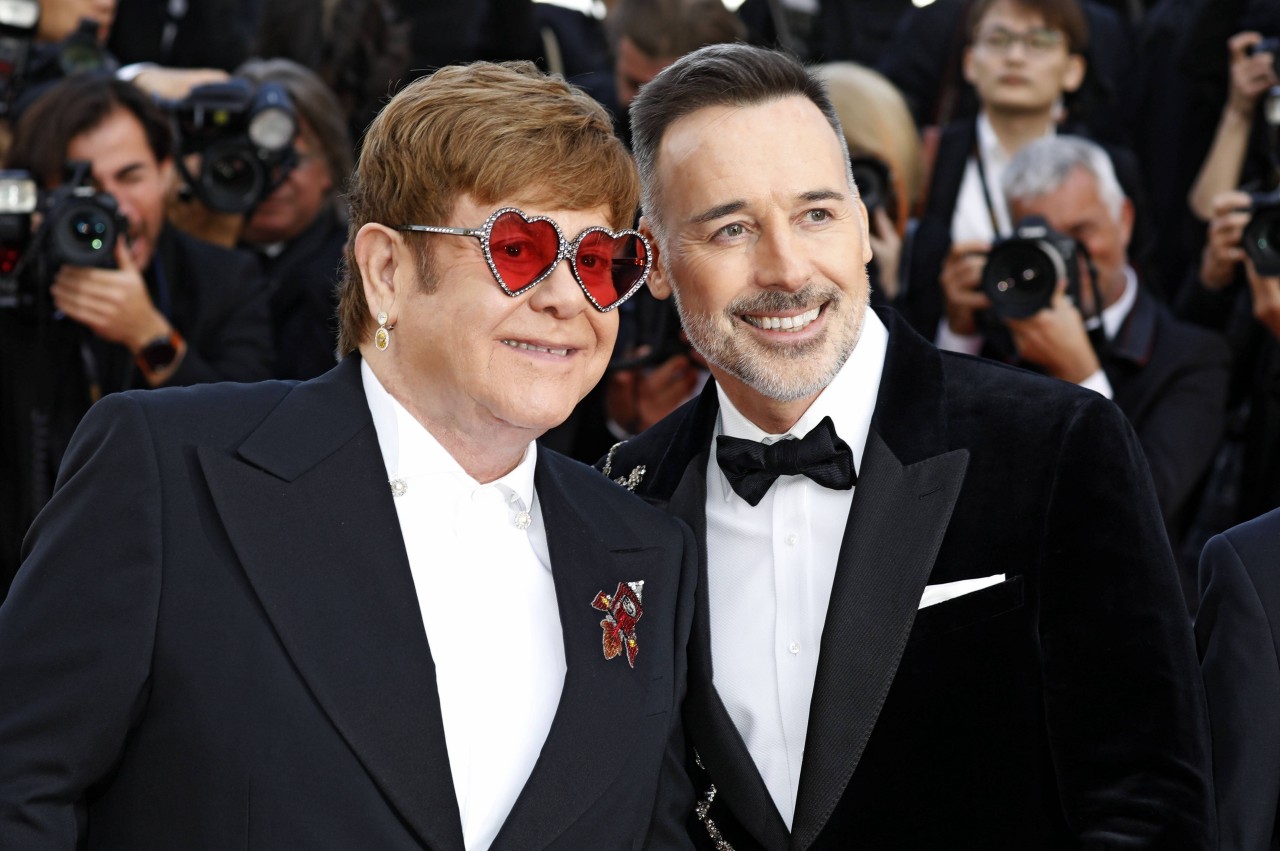 Meghan wird mit Elton Johns (l.) Ehemann David Furnish (r.) zusammenarbeiten.