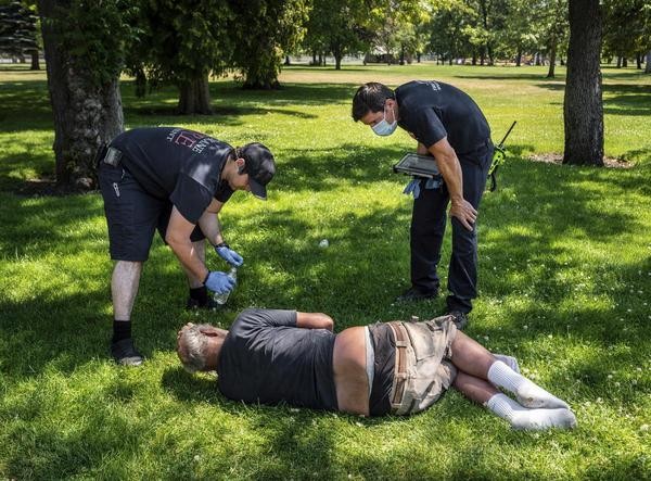USA, Spokane: Feuerwehrmann Sean Condon (l) und Leutnant Gabe Mills überprüfen das Wohlergehen eines Mannes im Mission Park. Viele Menschen kollabieren wegen der Hitzewelle.