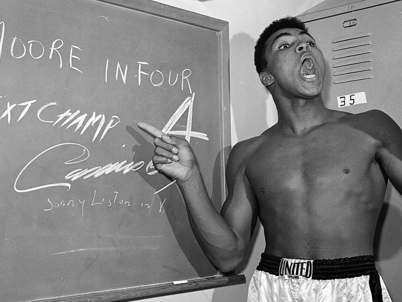 1962: Cassius Clay als Prophet. Auf einer Tafel schrieb er auf, in welcher Runde er Kontrahent Archie Moore auf die Bretter schicken möchte.(AP Photo/Harold P. Matosian, File)