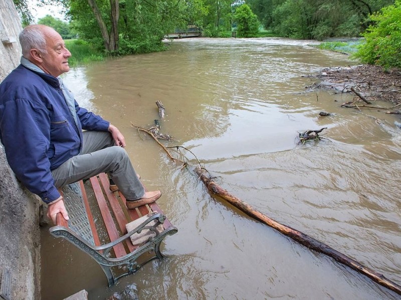 Peter Burckhardt sitzt auf einer Bank in seinem Garten in Taubach, Thüringen, durch den die über die Ufer getretene Ilm fließt.