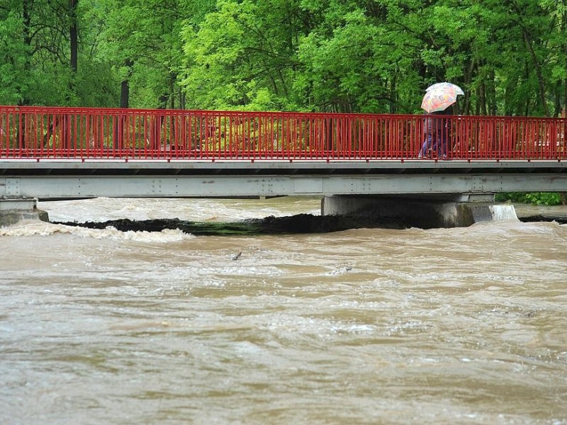Überflutung in Bischleben, Thüringen: Zwei Menschen gehen mit Regenschirm in Erfurt-Bischleben über die Brücke an der Zaunwiese.