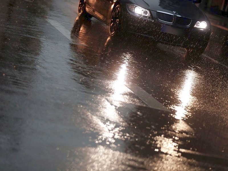 Autos fahren tagsüber mit Abblendlicht durch den Regen.