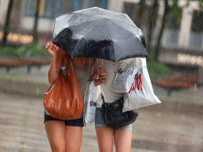 Zwei junge Damen gehen in Köln untern einem Schirm durch den Regen.
