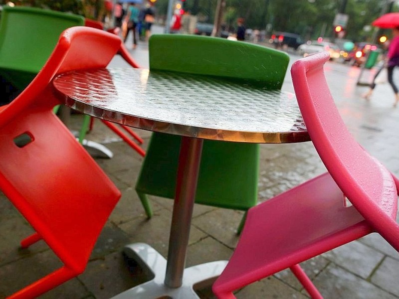 Hinter zusammengestellten Stühlen läuft eine Frau im Regen über eine Straße in Düsseldorf.