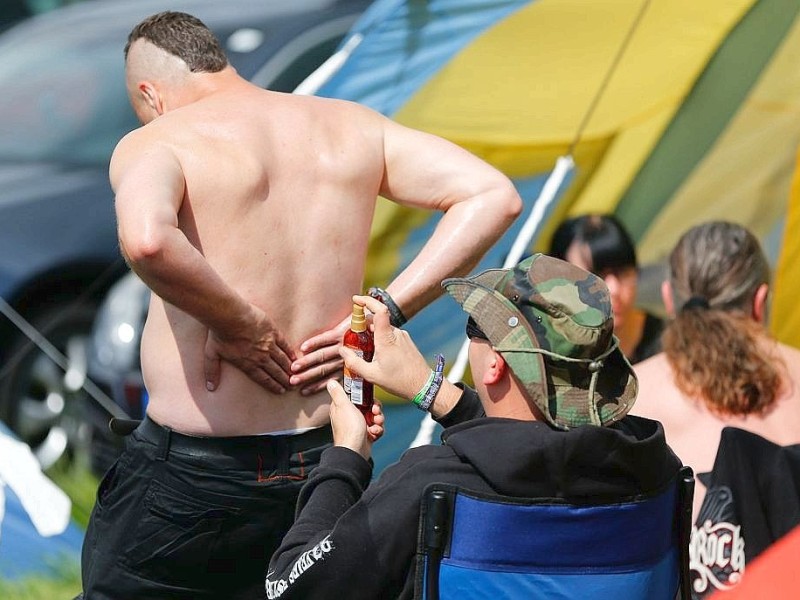 Besucher des Wacken-Open-Air-Festivals cremen sich auf dem Festivalgelände mit Sonnencreme ein.