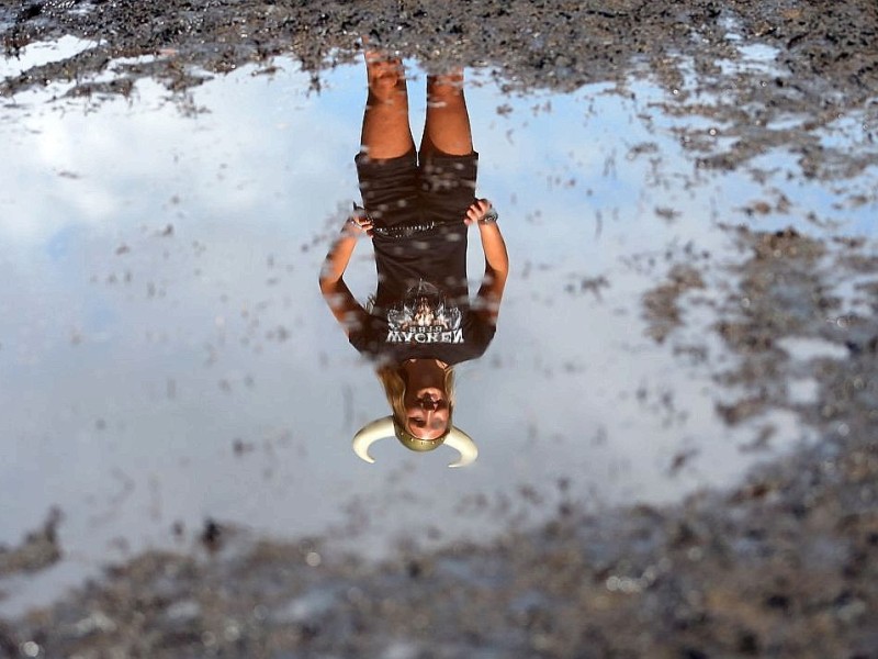 Eine Besucherin des Wacken-Open-Air-Festivals spiegelt sich in einer Schlammpfütze auf dem Festivalgelände.