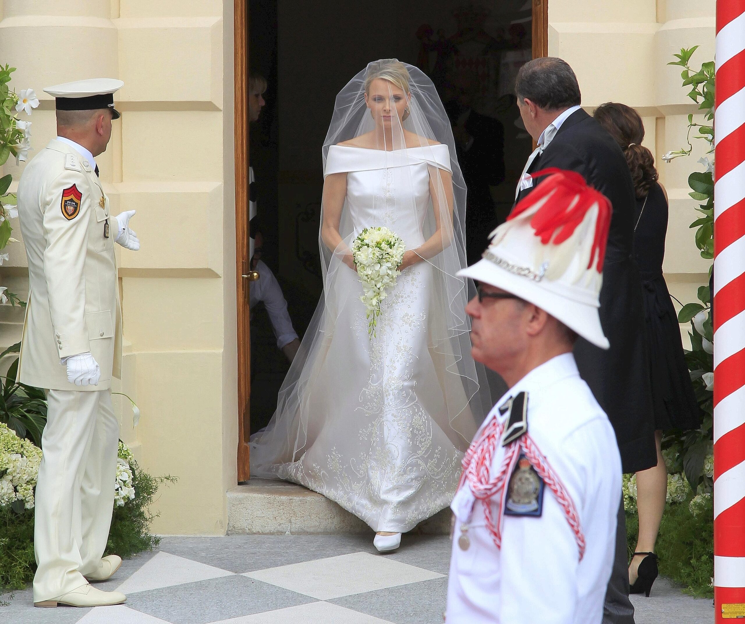 Charlene trägt ein schlichtes weißes Kleid mit langer Schleppe. Entworfen wurde es von Armani.