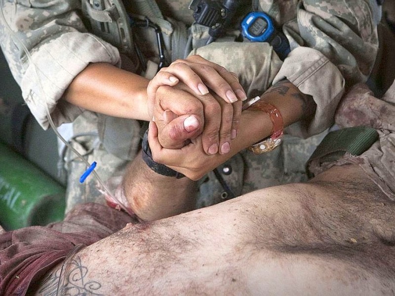 Eine Soldatin hält die Hand des Verletzten.