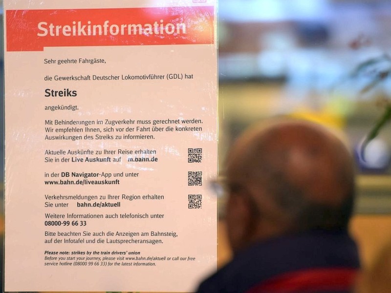 Fahrgäste der Bahn lesen im Hauptbahnhof in Köln ein Plakat mit Streikinformationen.
