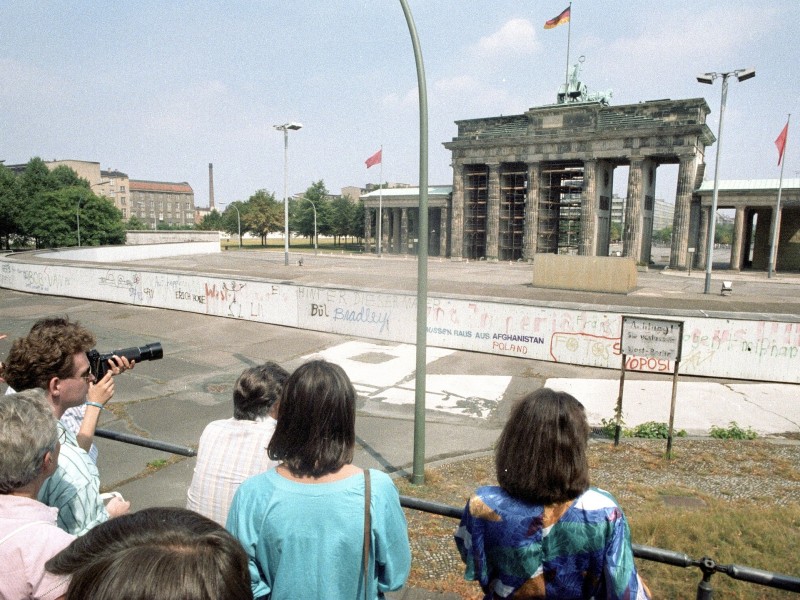 Passanten auf der West-Berliner Seite vor der Mauer am Brandenburger Tor vor der Wende ...