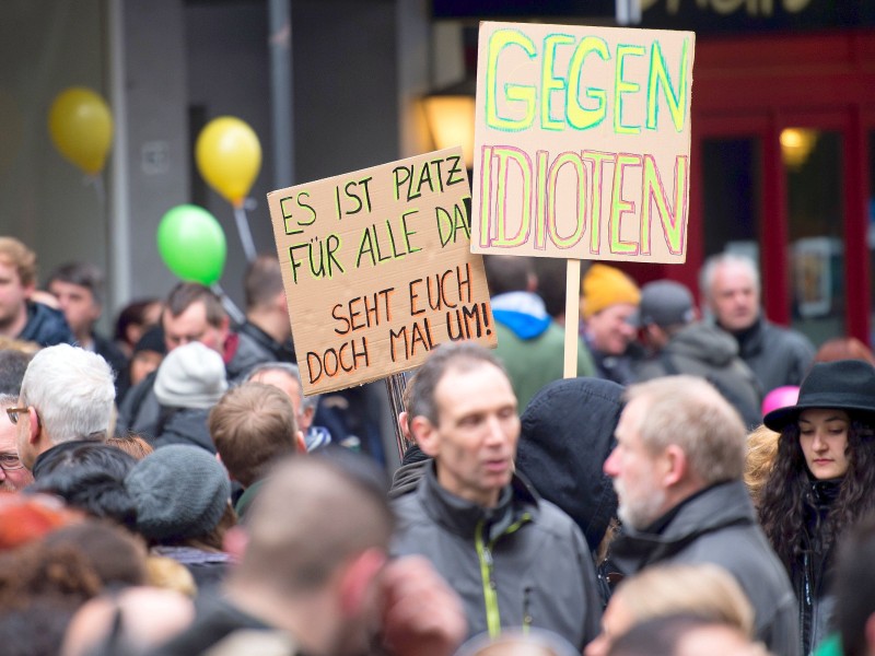 Demonstranten halten Schilder mit der Aufschrift Gegen Idioten und Es ist Platz für alle da, um damit gegen extremistische Demos in der Stadt zu protestieren.