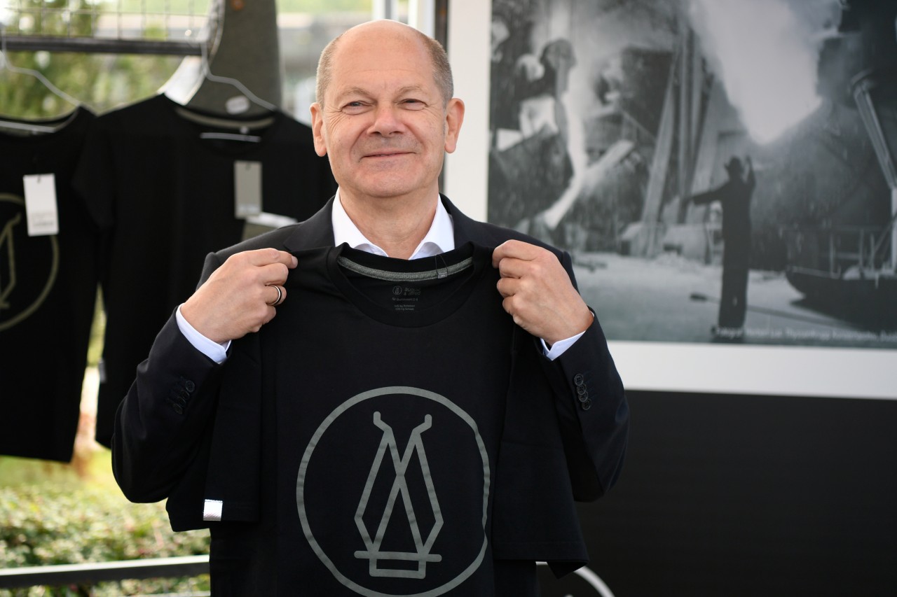 Olaf Scholz hält bei seinem Besuch bei Thyssenkrupp Steel Europe AG ein T-Shirt von august & alfred hoch, der Marke des Stahlherstellers.