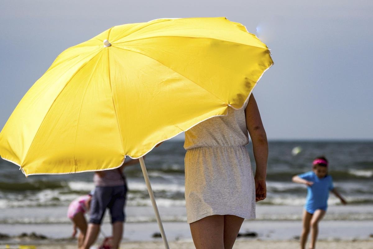 Eine Frau stellt in der gleißenden Sonne am Strand von St. Peter-Ording einen Sonnenschirm auf.