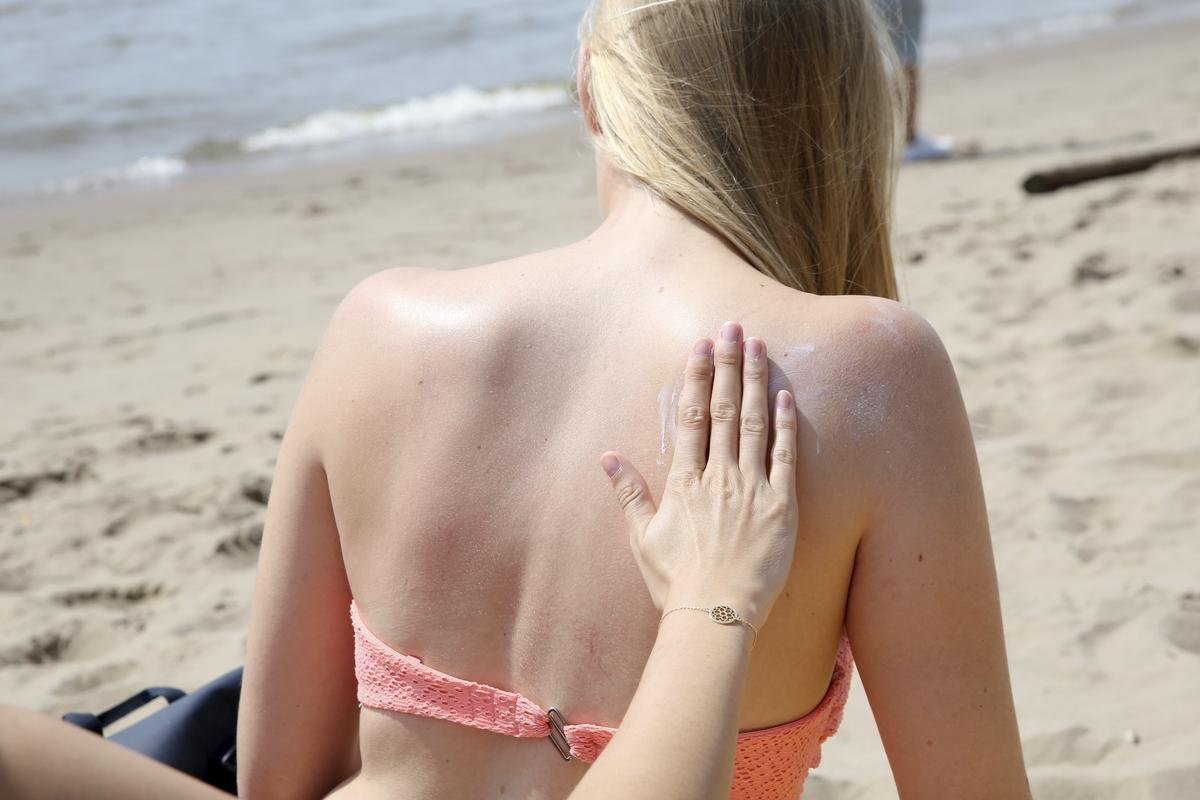 Eine junge Frau wird bei hochsommerlichen Temperaturen am Strand von ihrer Freundin mit Sonnencreme eingerieben. Zig Tonnen Sonnencreme landen jährlich in Gewässern - das hat Folgen für die Lebewesen dort, wie Untersuchungen zeigen.