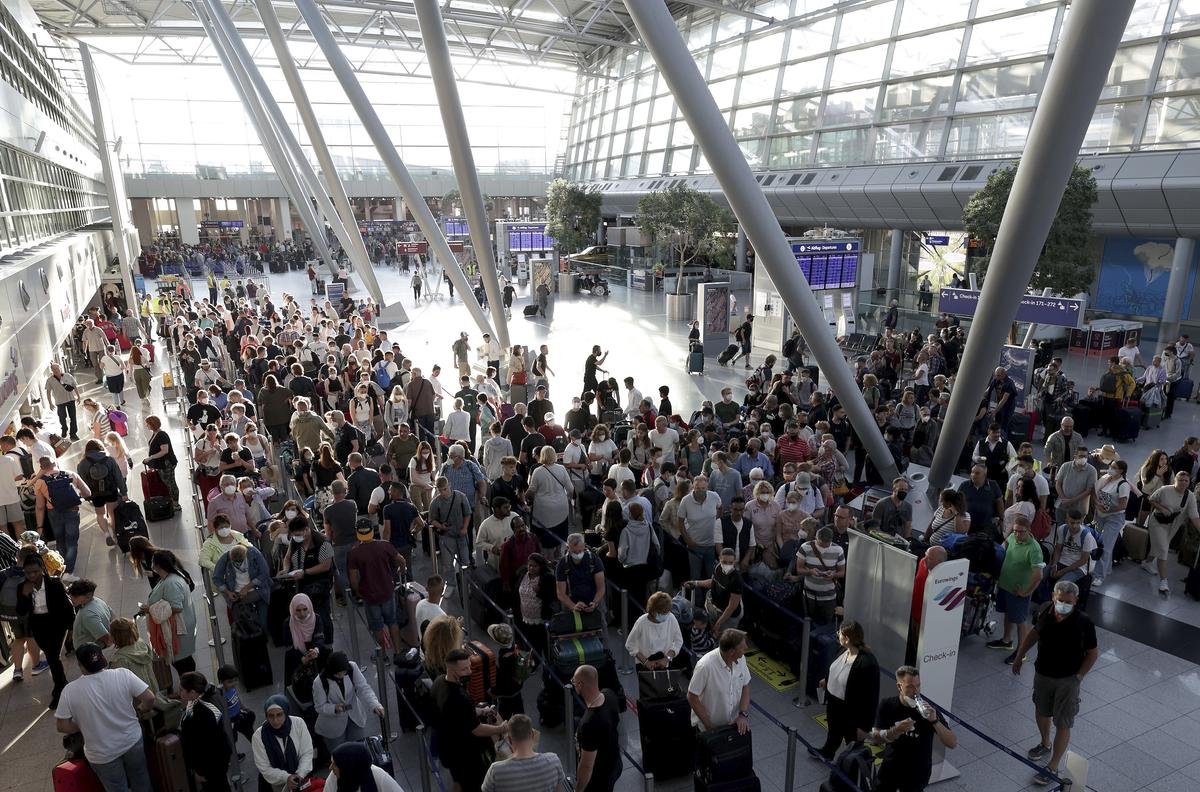 Passagiere stehen vor den Schaltern im Flughafen Düsseldorf in Schlangen und warten auf die Abfertigung. Als erstes Bundesland ist Nordrhein-Westfalen am Freitag in die Ferien gestartet.