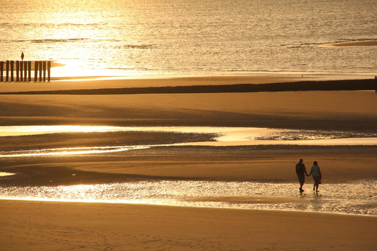 Spaziergänger gehen in der Abendsonne am Strand von Wangerooge. Zur Mittsommerzeit bietet die ostfriesische Insel spezielle Angebote für Sonnenhungrige an.