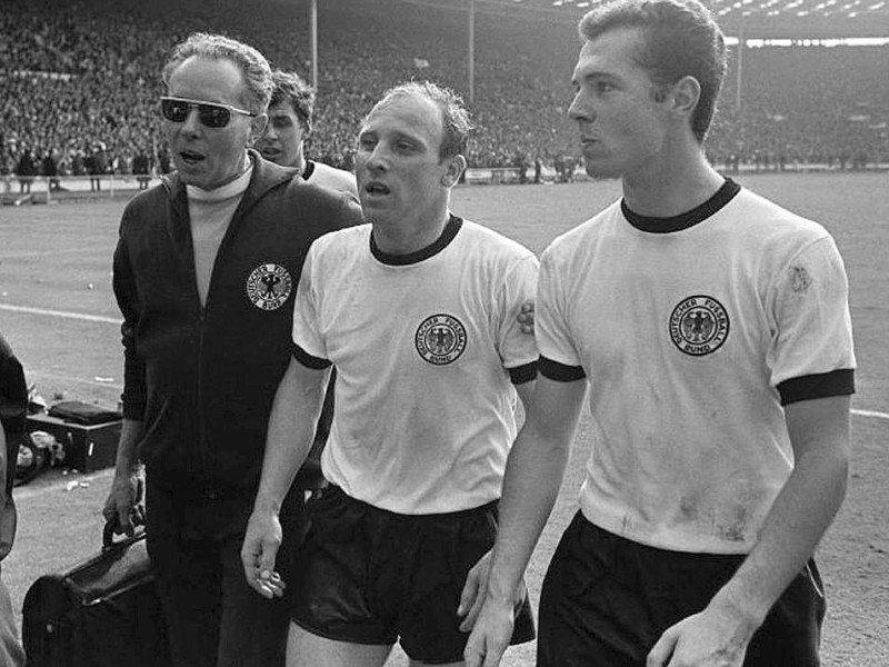 ...nur im Finale trugen sie wieder ein Trikot mit Rundkragen. Dieses Bild zeigt Masseur Erich Deuser (li.) mit Uwe Seeler (Mitte) und Franz Beckenbauer in der Halbzeitpause beim legendären Wembley-Finale, das Deutschland nach dem umstrittensten Tor aller Zeiten mit 4:2 verlor.