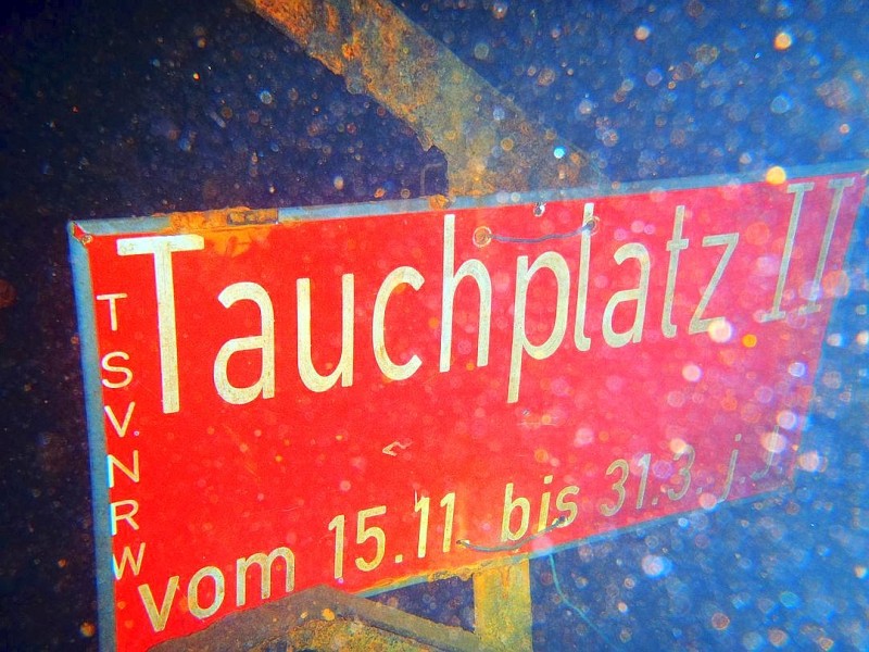 Ein Schild unter Wasser weist den Weg zum Tauchplatz.