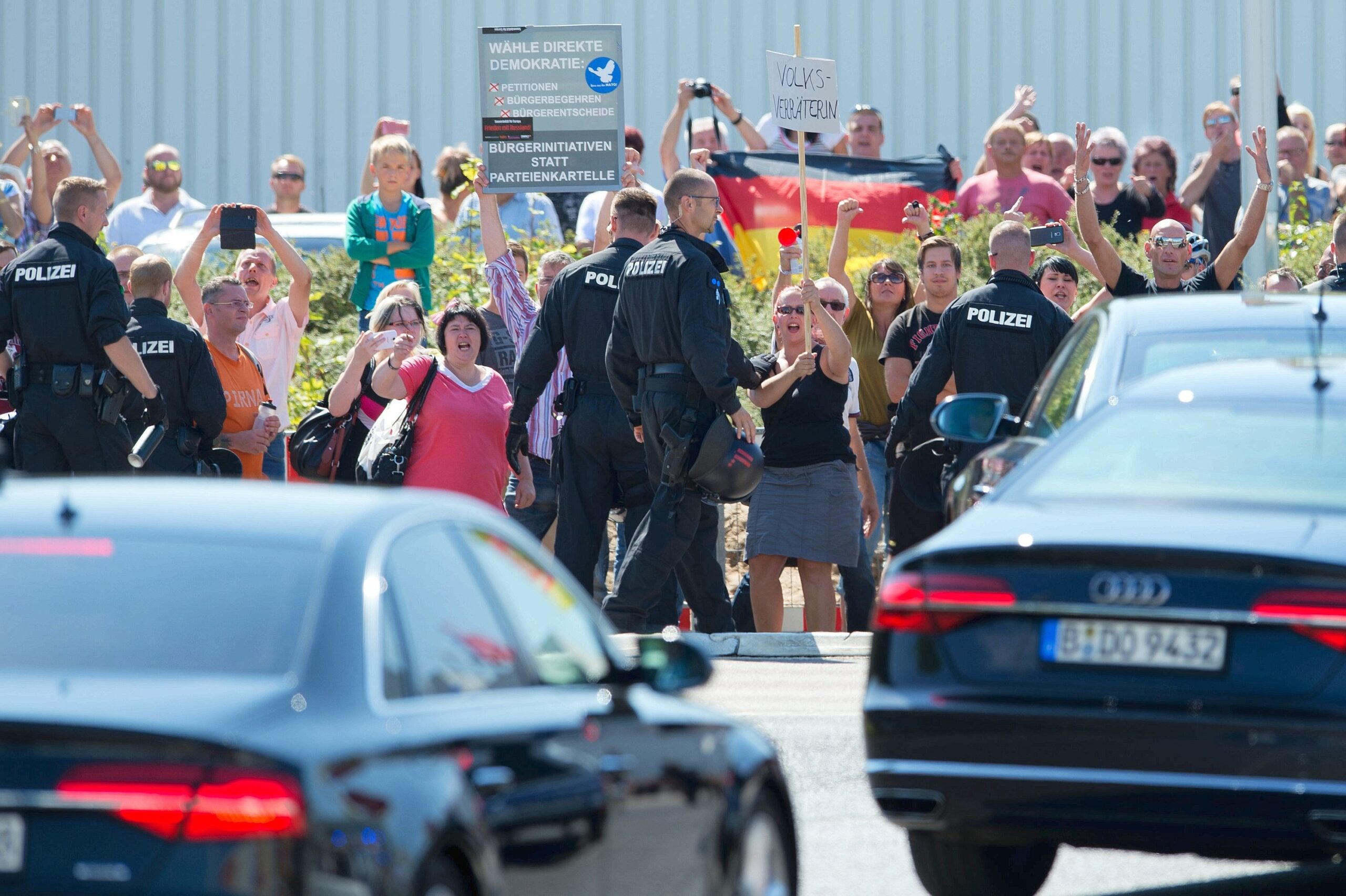Die Fahrzeugkolonne der Bundeskanzlerin verlässt Heidenau unter dem Schutz der Polizei und unter dem Protest zahlreicher Bürger, die am Straßenrand stehen.