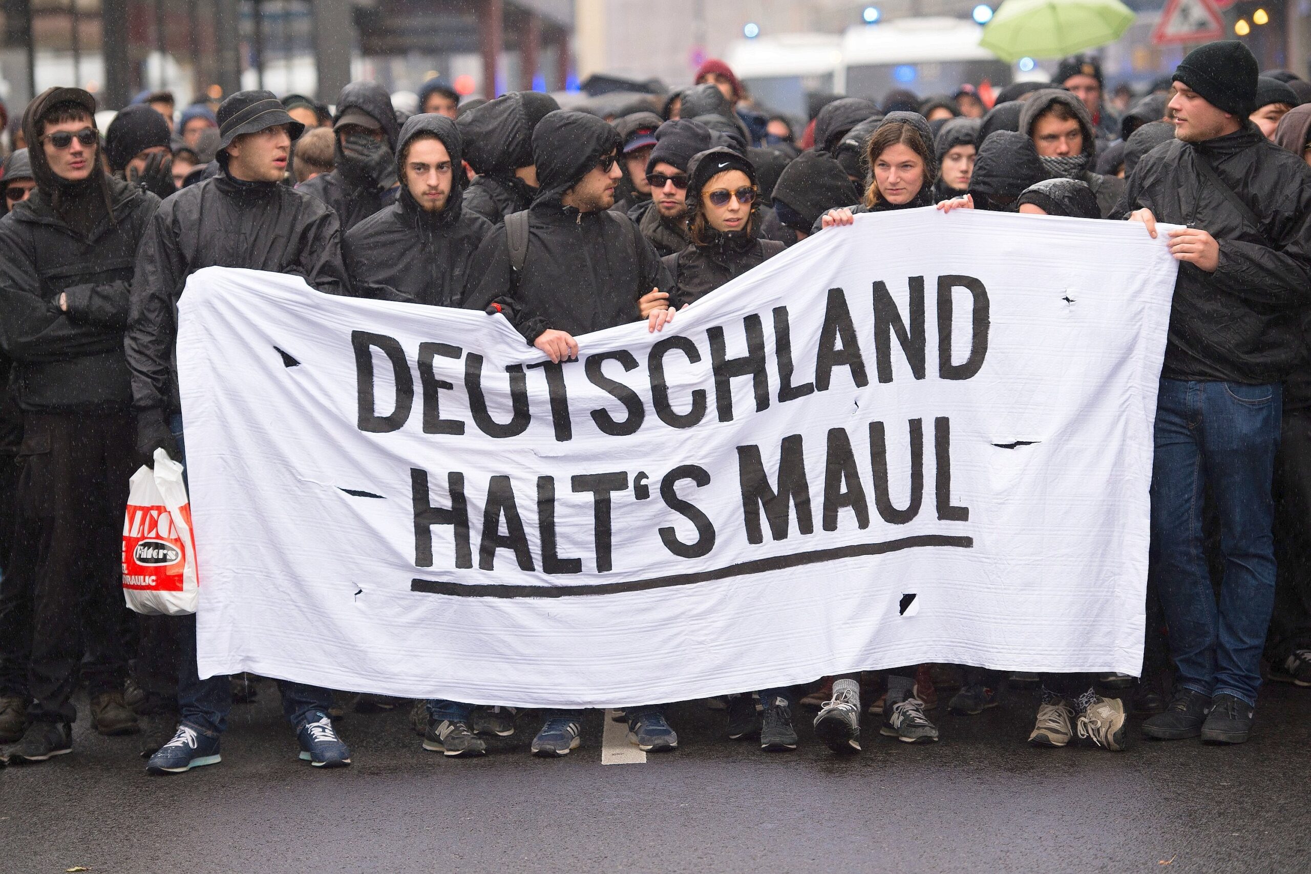 Teilnehmer einer linken Demonstration auf dem Heumarkt in Köln. Sie halten ein Banner mit der Aufschrift ´Deutschland halt's Maul».